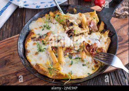 Gebratene Pasta mit Rührei, roten Zwiebeln, Schinken und Mozzarella-Käse in einer Pfanne Stockfoto