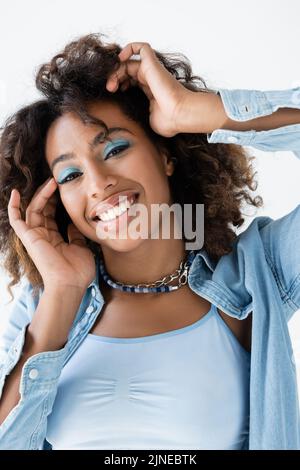 Glückliche afroamerikanische Frau mit blauen Lidschatten und perfekter Haut isoliert auf Weiß Stockfoto