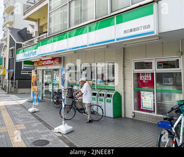 Eine Außenaufnahme eines FamilyMart-Lebensmittellauers mit Mülltonnen und Werbeflaggen vor dem Haus befindet sich im ersten Stock eines Mehrfamilienhauses. Stockfoto