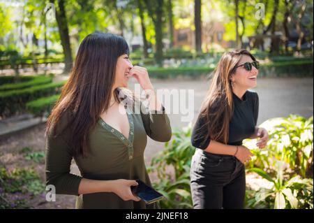 Zwei Freundinnen, die im Park spazieren und lachen Stockfoto