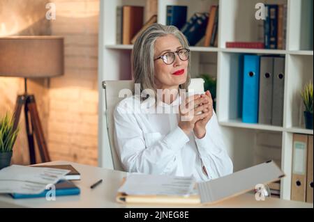 Elegante reife Frau mit Kaffee und suchen friedlich Stockfoto