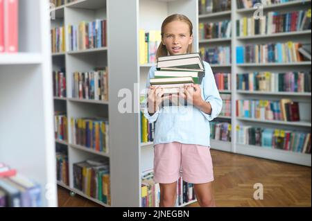 Unzufriedene Schülerin, die einen Stapel Bücher in ihren Händen hielt Stockfoto