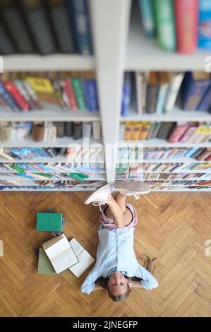 Fröhliches Teenager-Mädchen, das sich in der Bibliothek ausruhte Stockfoto