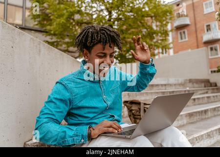 Kerl winkt mit der Hand und schaut auf den Laptop auf der Straße Stockfoto