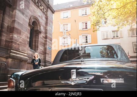 Straßburg, Frankreich - 12. Sep 2015: Rückansicht einer alten, schwarzen Luxuslimousine von Rolls-Royce Silver Wraith in der Stadt, in der eine junge Frau auf dem Smartphone auf der Straße spricht Stockfoto