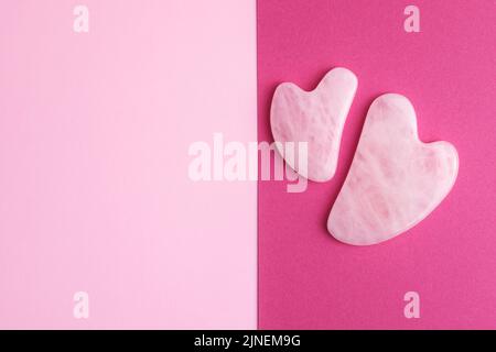 Rosenquarz-Gesichtsmassagesteine auf zweifarbigem rosa und purpurem Hintergrund mit leerem Raum für Ihr Design. Stockfoto
