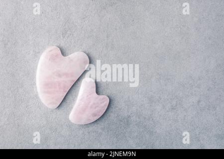 Rosenquarz Gua Sha Steine unterschiedlicher Größe auf grauem Steingrund mit Kopierraum. Stockfoto