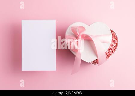 Leere Karte und festliche Geschenkbox isoliert auf pastellrosa Hintergrund. Baby-Dusche, Muttertag, Valentinstag Gruß Mock-up. Stockfoto