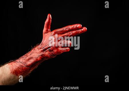 Blutige männliche Hand zeigt eine Waffe vor schwarzem Hintergrund. Stockfoto