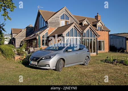 Metallisch graues Nissan Leaf e-connecta EV-Elektroauto, das vor dem Ökohaus Cotswolds in Großbritannien geparkt ist Stockfoto