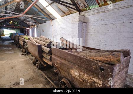 Kleine, rostige, alte Eisenbahn, mit Holzstämmen beladene Zugwagen, bereit, zur Mine zu fahren. Im Big Pit National Coal Museum in Pontypool, Wales, Vereinigtes Königreich Stockfoto