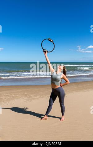 Junge Sportlerin posiert mit Pilates Ring am Strand Stockfoto