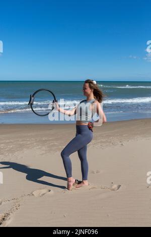 Schöner Athlet mit Pilates Ring am Strand posiert Stockfoto