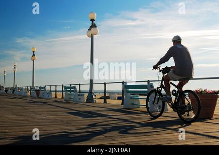 Ein männlicher Radfahrer fährt am frühen Morgen mit dem Fahrrad auf der Promenade in Avon by the Sea an der Küste von New Jersey, um sich zu bewegen und gesund zu leben Stockfoto