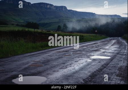 Eine Straße, die sich nach einem Winterregen durch das südafrikanische Kamberg Valley in den Drakensberg-Bergen schlängelt Stockfoto