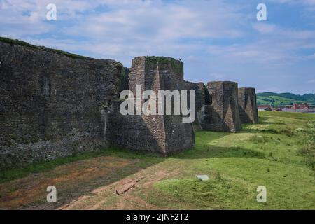 Blick auf die äußeren Steinmauer Befestigungen und Türmchen mit dem trockenen Graben, jetzt Rasen, Gras. In Caerphilly Castle in Caerphilly, Großbritannien. Stockfoto