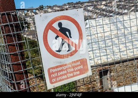 Ein Sicherheitshinweis, der die Passagiere warnt, die Linie am Ende eines Bahnsteigs am Dockyard-Bahnhof, Morice Town, Plymouth, nicht zu überqueren Stockfoto