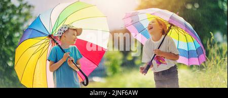 Glückliche Kinder stehen unter dem Regen mit bunten Regenschirmen in den Händen. Stockfoto