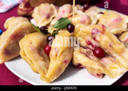 Ukrainische Varenyky mit Kirschen in einer weißen Platte aus weißer Tischdecke. Hartes Licht. Selektiver Fokus. Nahaufnahme Stockfoto