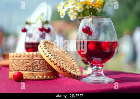 Süße Kirsche Tinktur in einem Glas mit Beeren auf dem Tisch und einer Holzkiste. Alkoholisches Nationales Getränk Stockfoto