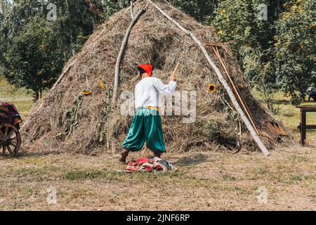 Ein Mann legt Heu in den Heuboden. Traditionelles Dorfleben in der Ukraine. nationalukrainische Kleidung. Alter Mann traditionelle Tracht Feld. Besticktes Hemd. Fa Stockfoto