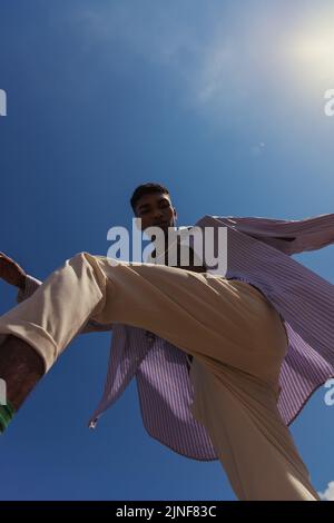 Bottom view of african american man posiert in trendigen Sommerkleidung unter blauem sonnigen Himmel, Stockbild Stockfoto