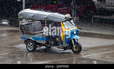 SAMUT PRAKAN, THAILAND, MAI 28 2022, Ein traditionelles Taxi-Motor-Dreirad - Tuk Tuk fährt auf einer Straße im Regen Stockfoto