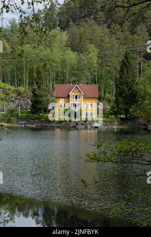 Wunderschöne Landschaften in Norwegen. Weste-Agder. Wunderschöne Landschaft einer gelben Villa, die sich im See spiegelt. Gräben. Berge und Bäume im Hintergrund Stockfoto