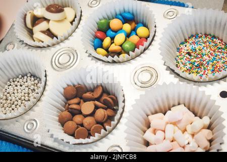 Schokoladen- und Süßwarenauflagen für süße Desserts oder Kuchen in Pappbecher-Kucheneinlagen auf einem Backblech Stockfoto