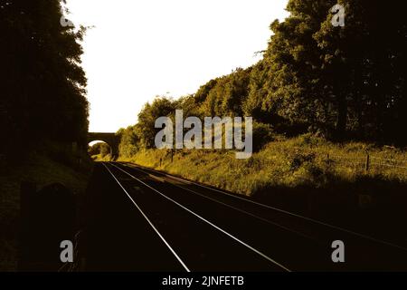 Bahnübergang in Lancashire für Fußgänger. Schauen Sie in beide Richtungen mit Eisenbahnbrücke im Sommer Abendlicht Stockfoto