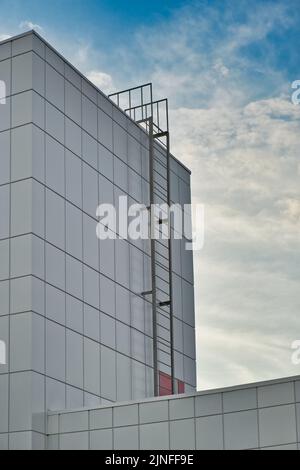 Feuerleiter zum Dach eines modernen Gebäudes aus Metallkonstruktionen. Feuertreppe an der Wand auf blauem Himmel Hintergrund. Stockfoto