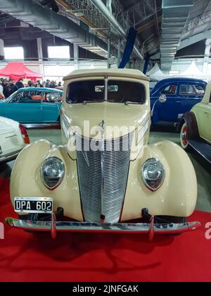 Altes antikes cremefarbenes Ford V8 Coupé Cabriolet Deluxe 1937 auf rotem Teppich. Vorderansicht. Chrom. Kühlergrill. Ausstellungshalle. Oldtimer-Show. Stockfoto