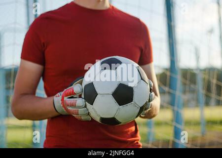 Porträt eines jungen Fußballspielers Torhüters mit Handschuhen, der den Fußball hält. Stockfoto