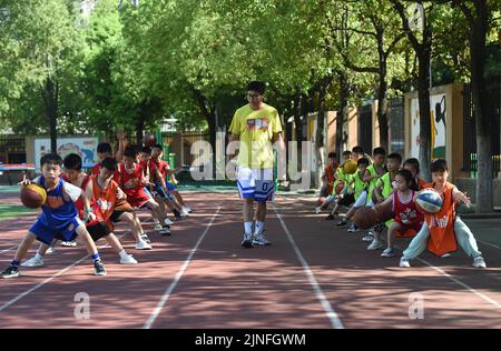 (220811) -- HEFEI, 11. August 2022 (Xinhua) -- Schüler lernen Basketball in Hefei, der ostchinesischen Provinz Anhui, zu spielen, 11. August 2022. Einige Schulen in Hefei bieten in diesem Sommer kostenlose Kindertagesstätten für Schüler an. Die Kindertagesstätten helfen nicht nur, die Sommerzeit der Schüler zu bereichern, sondern auch, den Druck auf berufstätige Eltern zu lockern, die sich sonst während der Ferien um ihre Kinder kümmern müssen. (Xinhua/Zhou Mu) Stockfoto