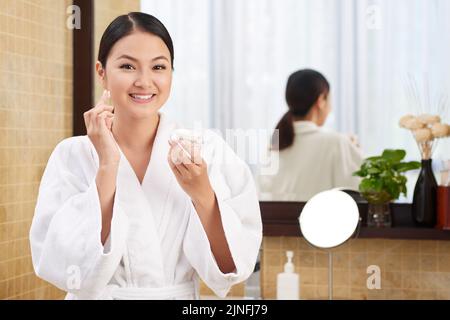 Lächelnde schöne Frau, die angereicherte Gesichtscreme anwendet Stockfoto