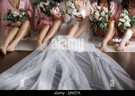 Braut mit Brautjungfern mit Blumen, die in einer Reihe sitzen. Stockfoto