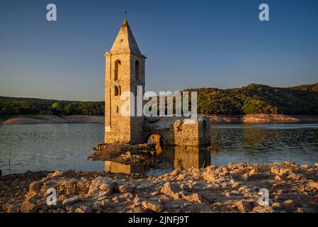 Sonnenaufgang am Glockenturm von Sant Romà de Sau und dem Stausee Sau während der Sommertrockenheit von 2022 (Osona, Barcelona, Katalonien, Spanien) Stockfoto