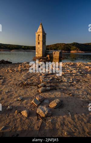 Sonnenaufgang am Glockenturm von Sant Romà de Sau und dem Stausee Sau während der Sommertrockenheit von 2022 (Osona, Barcelona, Katalonien, Spanien) Stockfoto