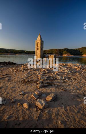 Sonnenaufgang am Glockenturm von Sant Romà de Sau und dem Stausee Sau während der Sommertrockenheit von 2022 (Osona, Barcelona, Katalonien, Spanien) Stockfoto