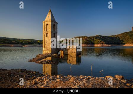 Sonnenaufgang am Glockenturm von Sant Romà de Sau und dem Stausee Sau während der Sommertrockenheit von 2022 (Osona, Barcelona, Katalonien, Spanien) Stockfoto