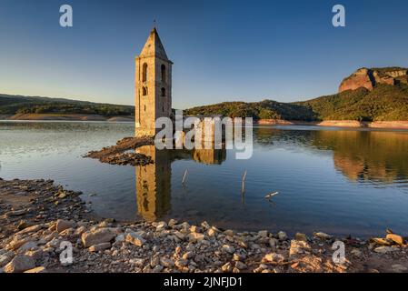 Sonnenaufgang am Glockenturm von Sant Romà de Sau und dem Stausee Sau während der Sommertrockenheit von 2022 (Osona, Barcelona, Katalonien, Spanien) Stockfoto