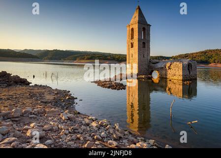 Sonnenaufgang am Glockenturm von Sant Romà de Sau und dem Stausee Sau während der Sommertrockenheit von 2022 (Osona, Barcelona, Katalonien, Spanien) Stockfoto