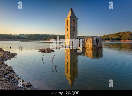 Sonnenaufgang am Glockenturm von Sant Romà de Sau und dem Stausee Sau während der Sommertrockenheit von 2022 (Osona, Barcelona, Katalonien, Spanien) Stockfoto