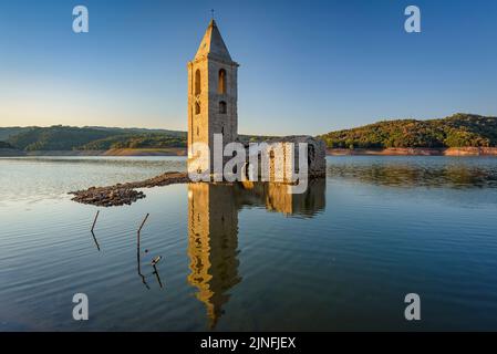 Sonnenaufgang am Glockenturm von Sant Romà de Sau und dem Stausee Sau während der Sommertrockenheit von 2022 (Osona, Barcelona, Katalonien, Spanien) Stockfoto