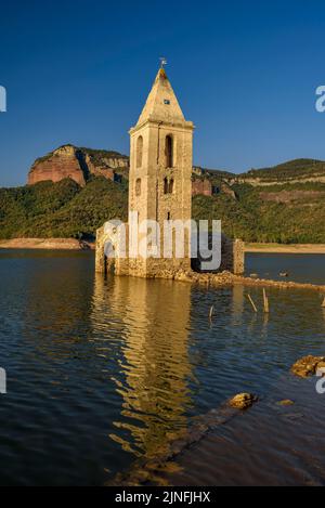 Sonnenaufgang am Glockenturm von Sant Romà de Sau und dem Stausee Sau während der Sommertrockenheit von 2022 (Osona, Barcelona, Katalonien, Spanien) Stockfoto