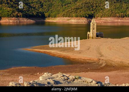 Sonnenaufgang am Glockenturm von Sant Romà de Sau und dem Stausee Sau während der Sommertrockenheit von 2022 (Osona, Barcelona, Katalonien, Spanien) Stockfoto