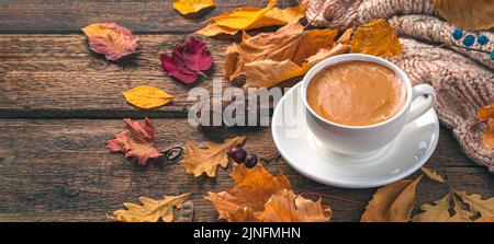 Kaffeetasse und Herbstlaub auf einem hölzernen Hintergrund. Gemütliche Herbstkomposition. Stockfoto