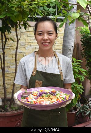 Vietnamesische Kellnerin serviert in der Pfanne gebratenes Huhn mit Gemüse im Café im Freien Stockfoto
