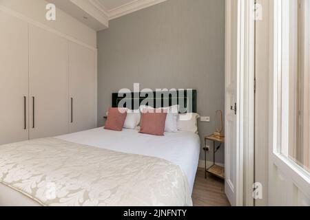 Doppelzimmer mit moderner Dekoration in der Ferienwohnung mit rosa Kissen und eingebautem Kleiderschrank mit weißen Holztüren Stockfoto