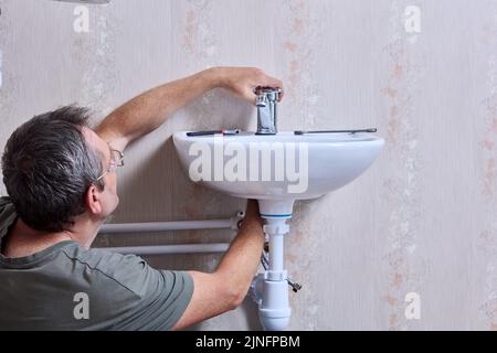 Sanitär arbeiten an der Installation neuer Wasserhahn in der Toilette, Klempner zieht Mutter, die Wasserhahn auf der Oberfläche des Waschbeckens sichert. Stockfoto